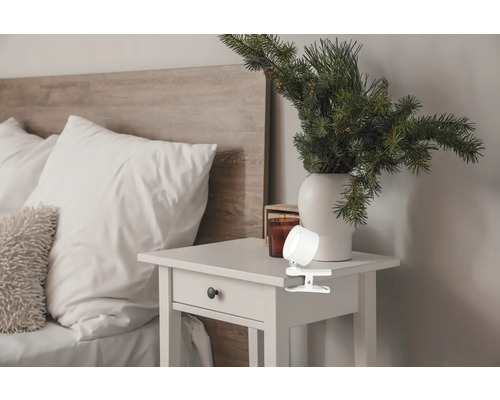 Klemmleuchte auf einem Nachttisch neben einem Bett mit Kopfende