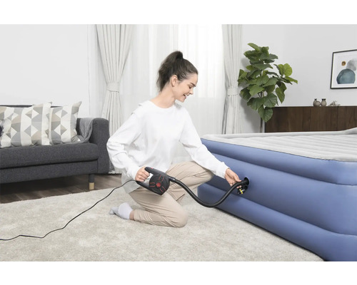 Frau pumpt Luftmatratze mit einer elektrischen Pumpe in einem hellen Wohnzimmer auf