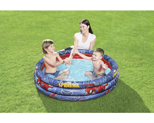 Aufblasbares Kinderplanschbecken mit Spiderman-Motiv im Garten mit spielenden Kindern und einer Frau.