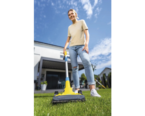 Frau benutzt einen Rasenkehrer im Garten vor einem Haus.