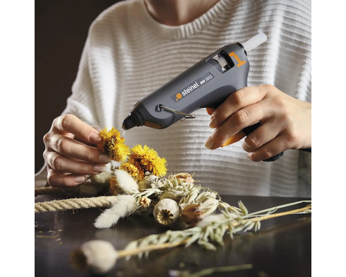 Anwender fixiert mit Heißklebepistole Blüten auf einem Kranz