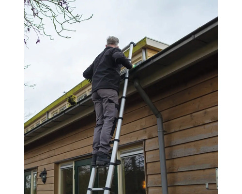 Mann reinigt Dachrinne mit einer Teleskopleiter an einem Haus.