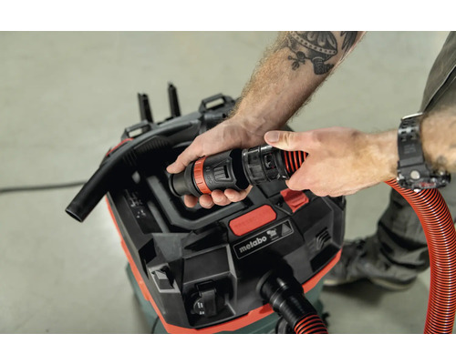 Eine Person befestigt einen flexiblen Staubsaugerschlauch an einem Metabo Staubsauger.