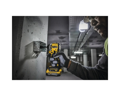 Ein Mann schraubt mit einem gelben DeWalt Akku-Schlagschrauber eine Schraube in eine Wand.