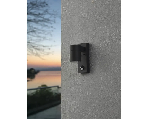 Schwarze Außenwandleuchte mit Bewegungsmelder an einer Wand montiert.