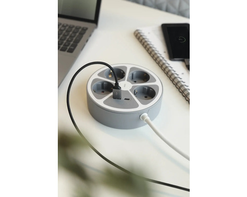 Runde Steckdosenleiste mit mehreren Anschlüssen und USB-Anschluss auf einem Schreibtisch.