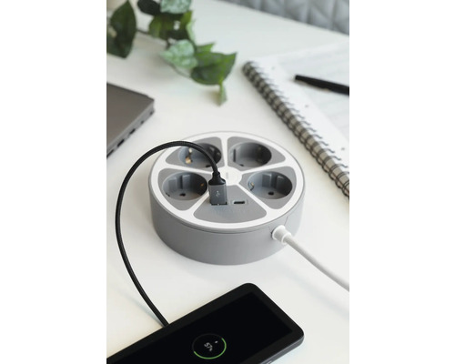 Runde Steckdosenleiste mit mehreren Anschlüssen und angeschlossenen Geräten auf einem Tisch.