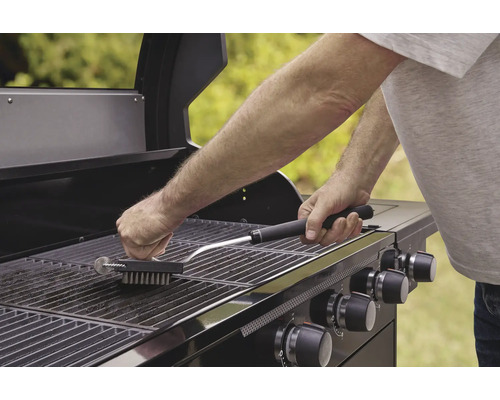 Eine Person reinigt einen Grillrost mit einer Grillbürste.
