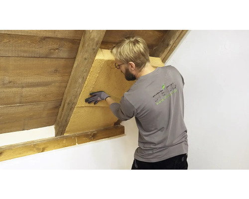 Ein Mann installiert eine Holzfaserdämmplatte in einem Dachgeschoss zur Dachdämmung.