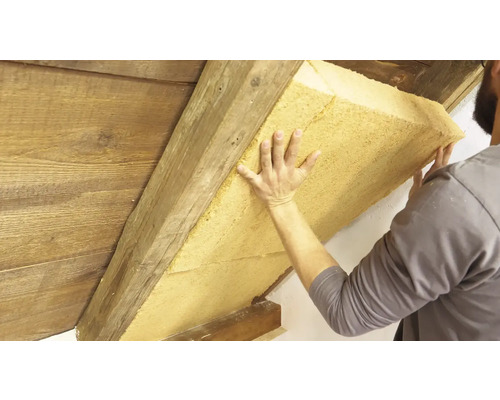 Ein Mann befestigt Dämmmaterial an einem Dachstuhl.