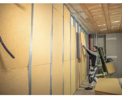 Ein Mann befestigt Holzfaserdämmplatten an einer Wandkonstruktion im Innenbereich.