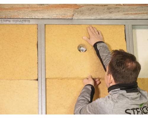 Ein Mann installiert Holzfaserdämmplatten zwischen Metallstreben an einer Wand.