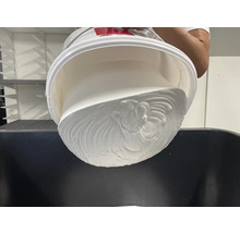 Ein weißer Eimer wird über einen Behälter entleert und gibt eine dicke, weiße Flüssigkeit frei.