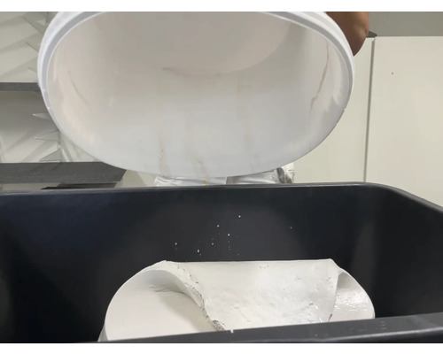 Eine Person schüttet Farbe aus einem Eimer in einen Farbbehälter.