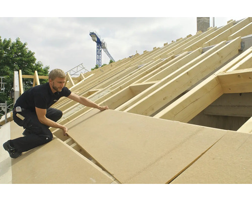 Handwerker verlegt Holzfaserplatten auf einem Dachstuhl.