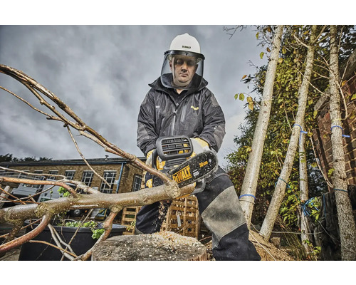 Eine Person mit Schutzkleidung und Schutzhelm sägt mit einer Akku-Kettensäge einen Ast ab. Im Hintergrund sind Bäume zu sehen.