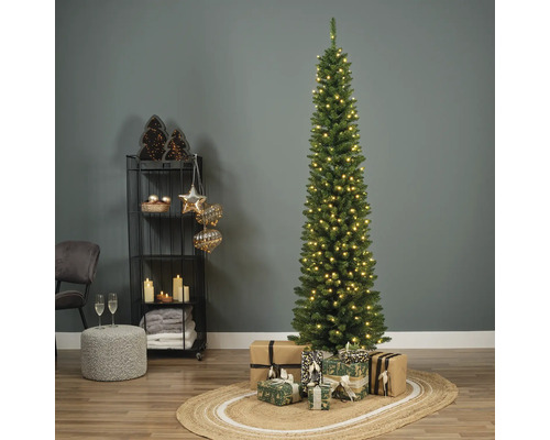 Schmaler, beleuchteter Weihnachtsbaum mit Geschenken auf einem Teppich in einem dekorierten Raum.