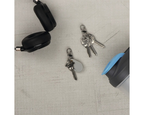 Drahtlose Kopfhörer, Schlüsselbund und Trinkflasche liegen auf einer ebenen Fläche.