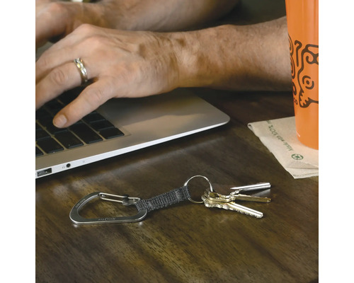 Schlüsselanhänger mit Karabiner auf einem Holztisch neben einem Laptop und einer Tasse.