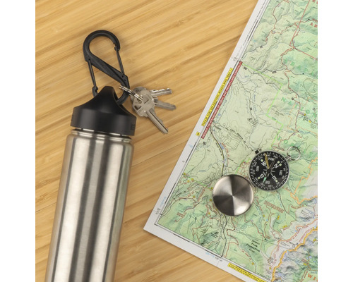Eine Edelstahl-Trinkflasche mit Karabinerhaken, Schlüsselbund, Kompass und einer Landkarte auf einem Holztisch.