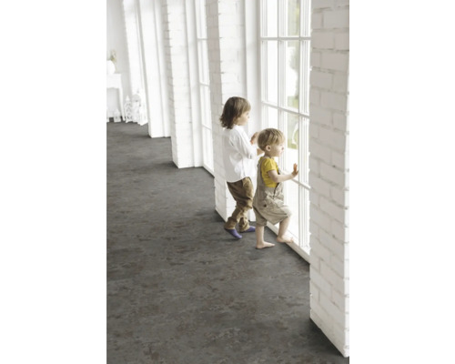 Kinder stehen an einem Fenster in einem hellen Raum mit dunklem Bodenbelag