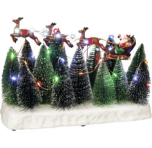 Dekoratives Weihnachtsdorf mit Weihnachtsmann im Schlitten, gezogen von Rentieren, inmitten von beleuchteten Tannenbäumen.