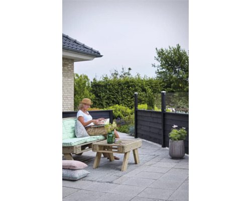 Terrassenszene mit Palisadenzaun, Palettenmöbeln und einer Frau, die ein Buch liest