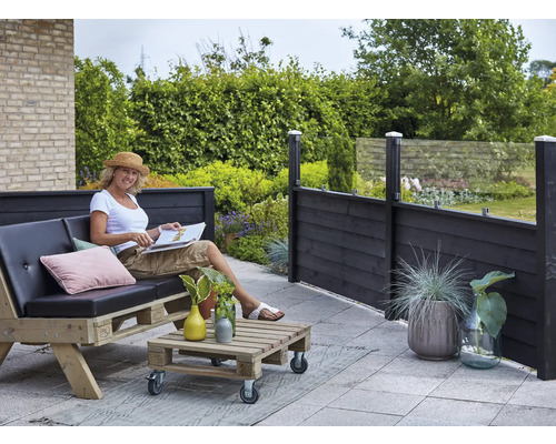 Terrassenszene mit Frau auf Palettensofa, Palettentisch und Sichtschutzzaun