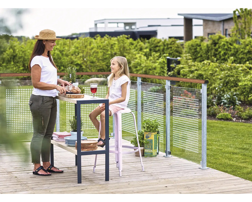 Szene auf einer Holzterrasse mit Mutter und Tochter, die Brot schneidet und auf einem Barhocker sitzt, mit einer Glasbalustrade im Hintergrund